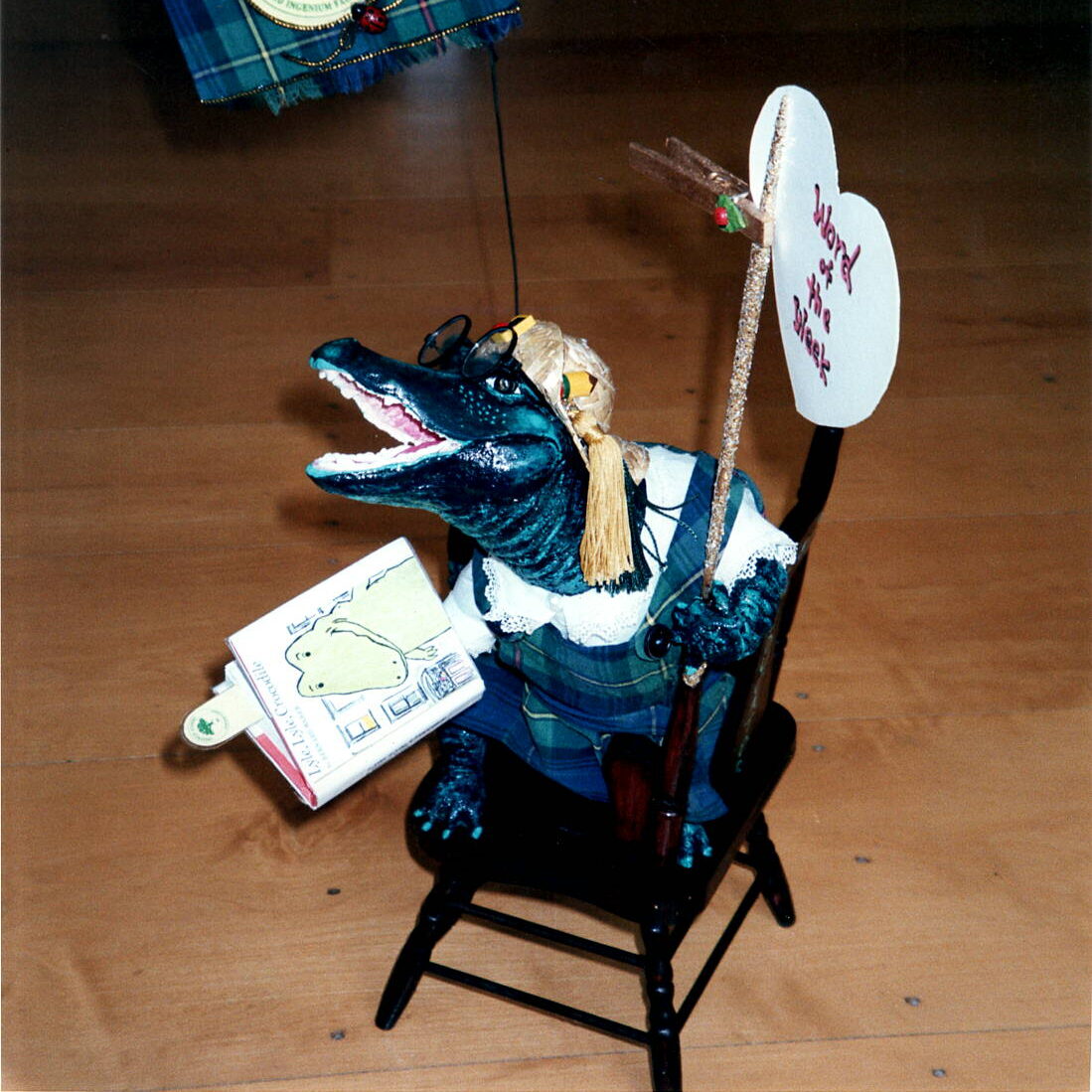 Ali the alligator sitting on a chair holding "Word of the Week" sign.
